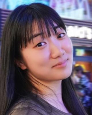 An Asian woman with long hair looks whimsically at the camera in front of a busy street.